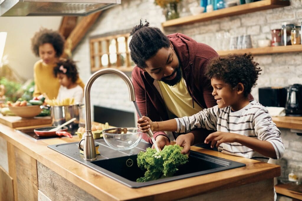 A man and child in the kitchen with broccoli.