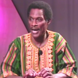 A man in colorful clothing talking on stage.