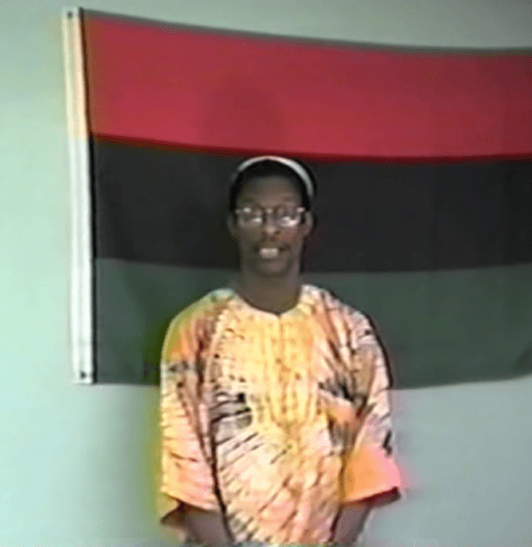 A man standing in front of a black and red flag.