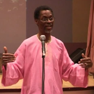 A man in pink shirt standing at microphone.