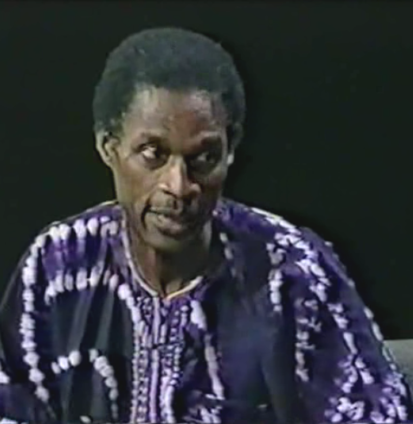 A man in purple and white shirt sitting down.
